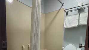A bathroom with a bathtub, toilet, and shower curtain. - Claremore Motor Inn (Claremore)