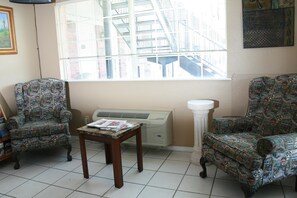 A room with two patterned armchairs, a small wooden table, a radiator, and a window with a city view.