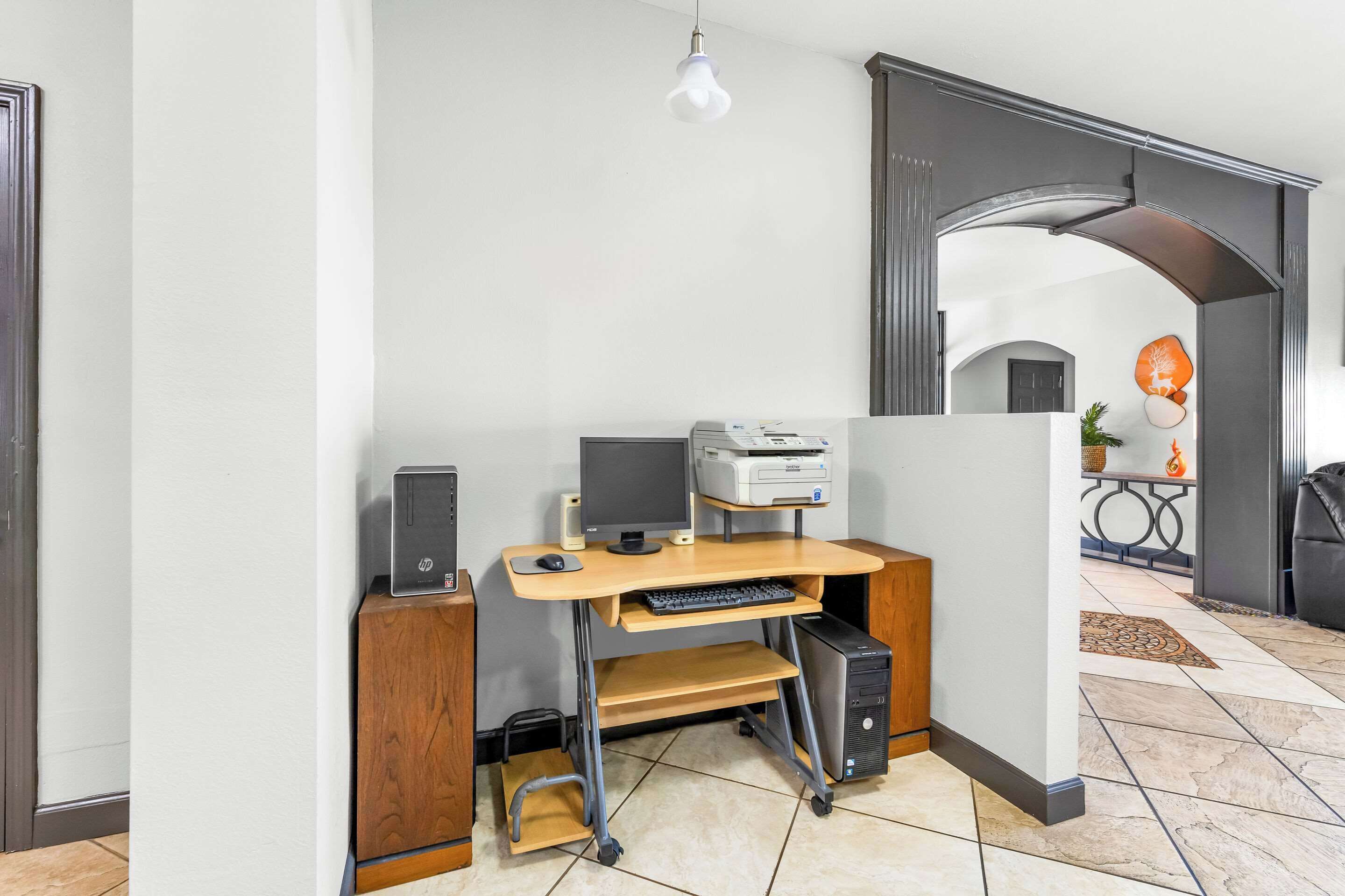 A home office setup with a desktop computer, printer, and monitor on a wooden desk.