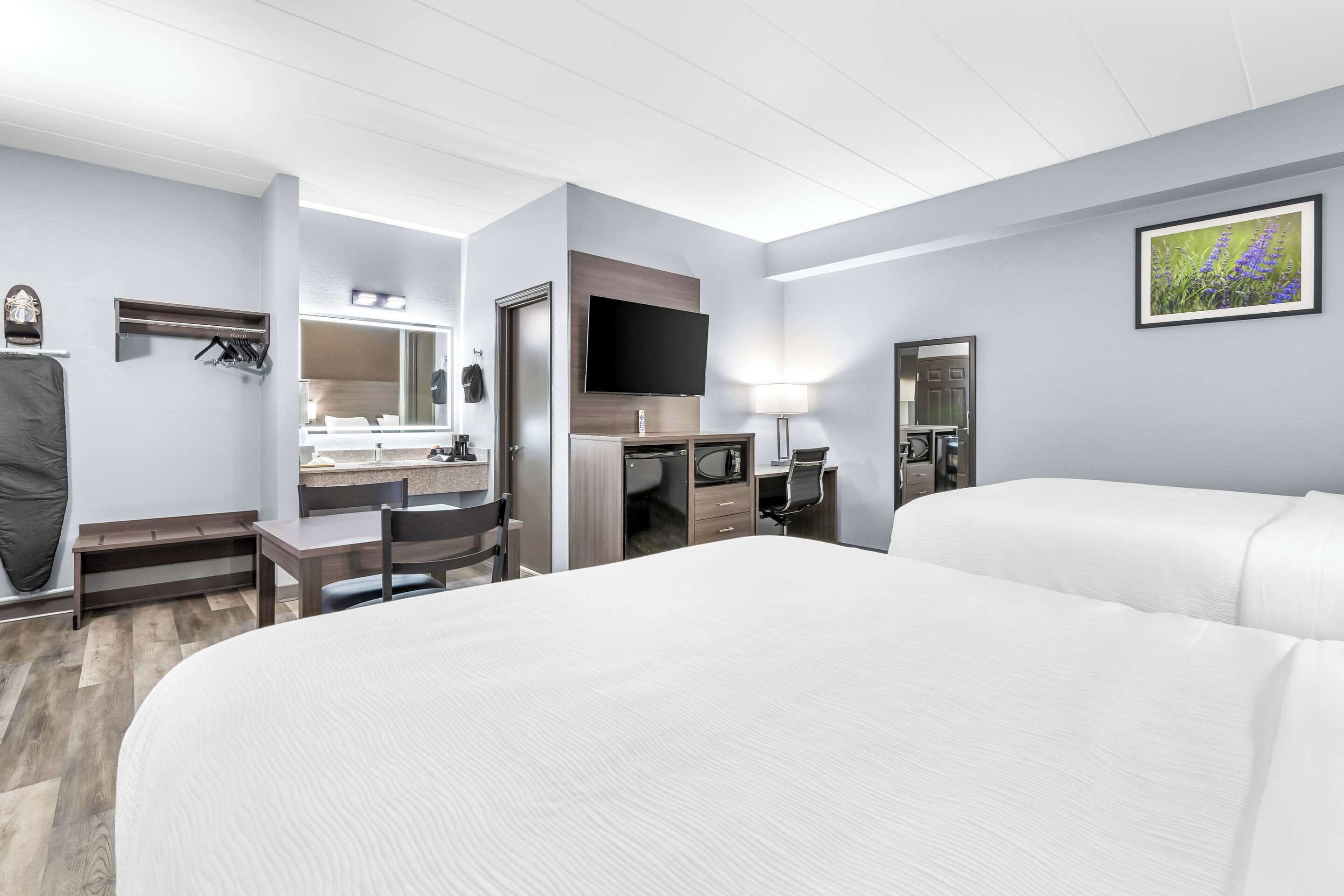 Una habitación de hotel con una cama grande, un escritorio con una silla, televisión, espejo y baño con ducha y retrete.