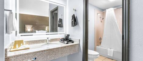 Et moderne badeværelse med bordplade i granit, et stort spejl, et toilet og en bruseniche med hvid gardin.