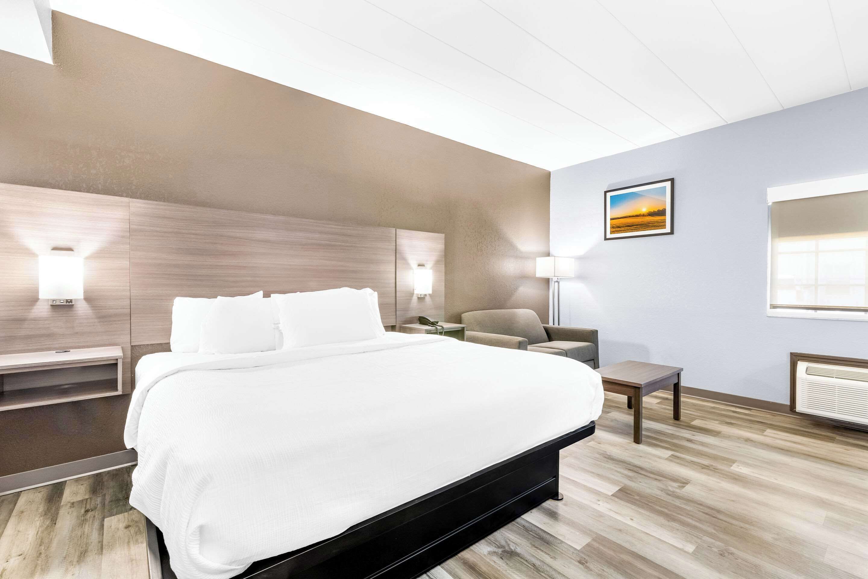 A modern hotel room with a large bed, bedside tables, a chair, a desk, and a picture on the wall.