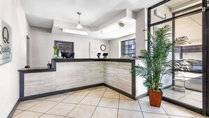 A reception area with a modern design, featuring a reception desk, a clock, and a large window offering a view of the street.