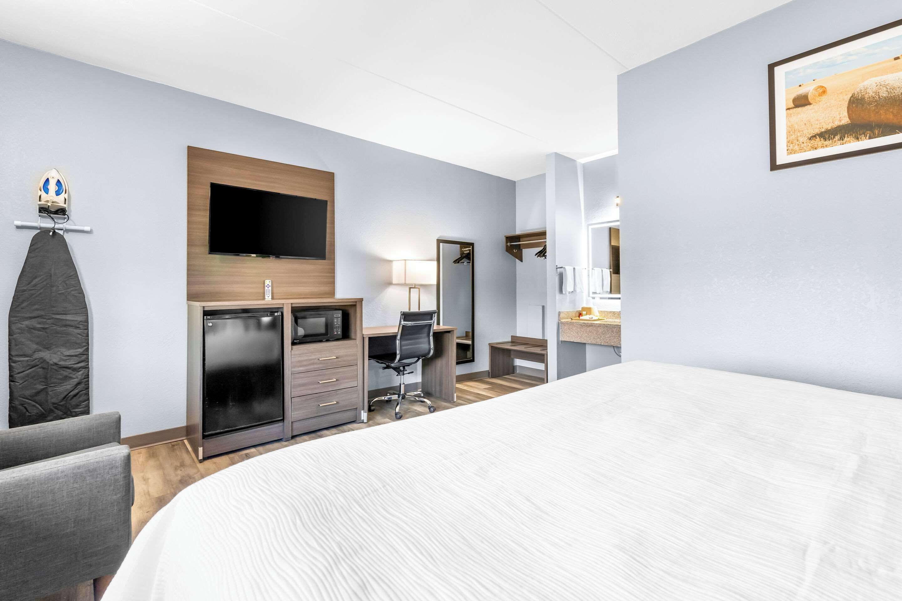 A hotel room with a bed, a desk with a computer, a TV, a mirror, and a microwave.