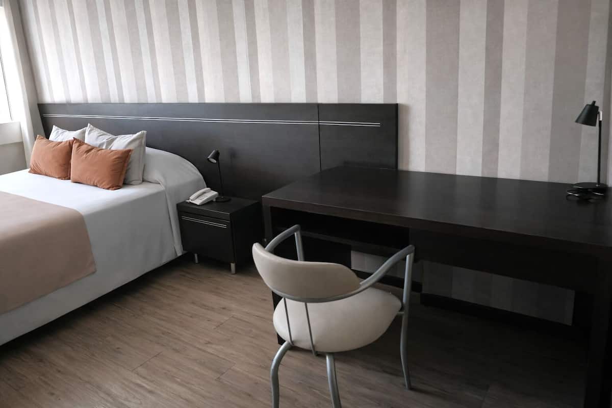 Una habitación de hotel con cama, mesita de noche, escritorio, silla y lámpara.