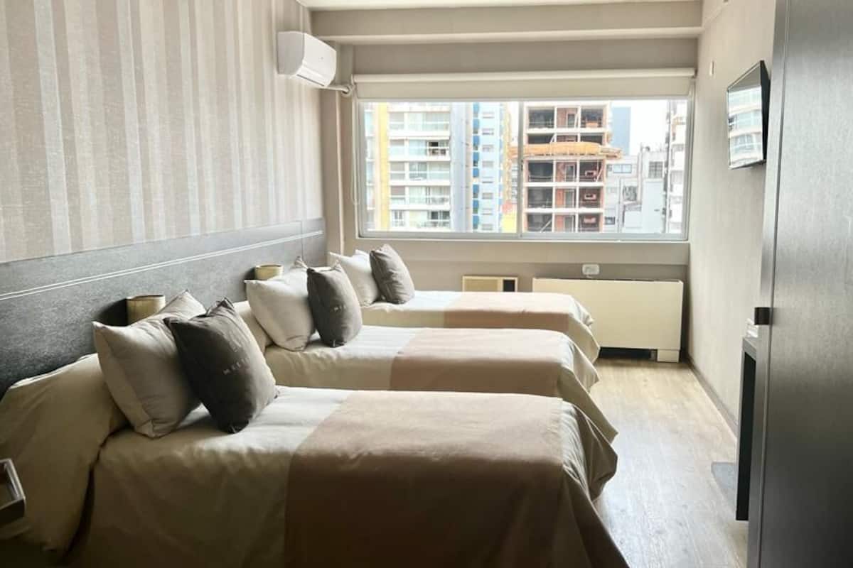 Habitación de hotel con dos camas, ventana con vista a la ciudad, televisor de pantalla plana y refrigerador incorporado.