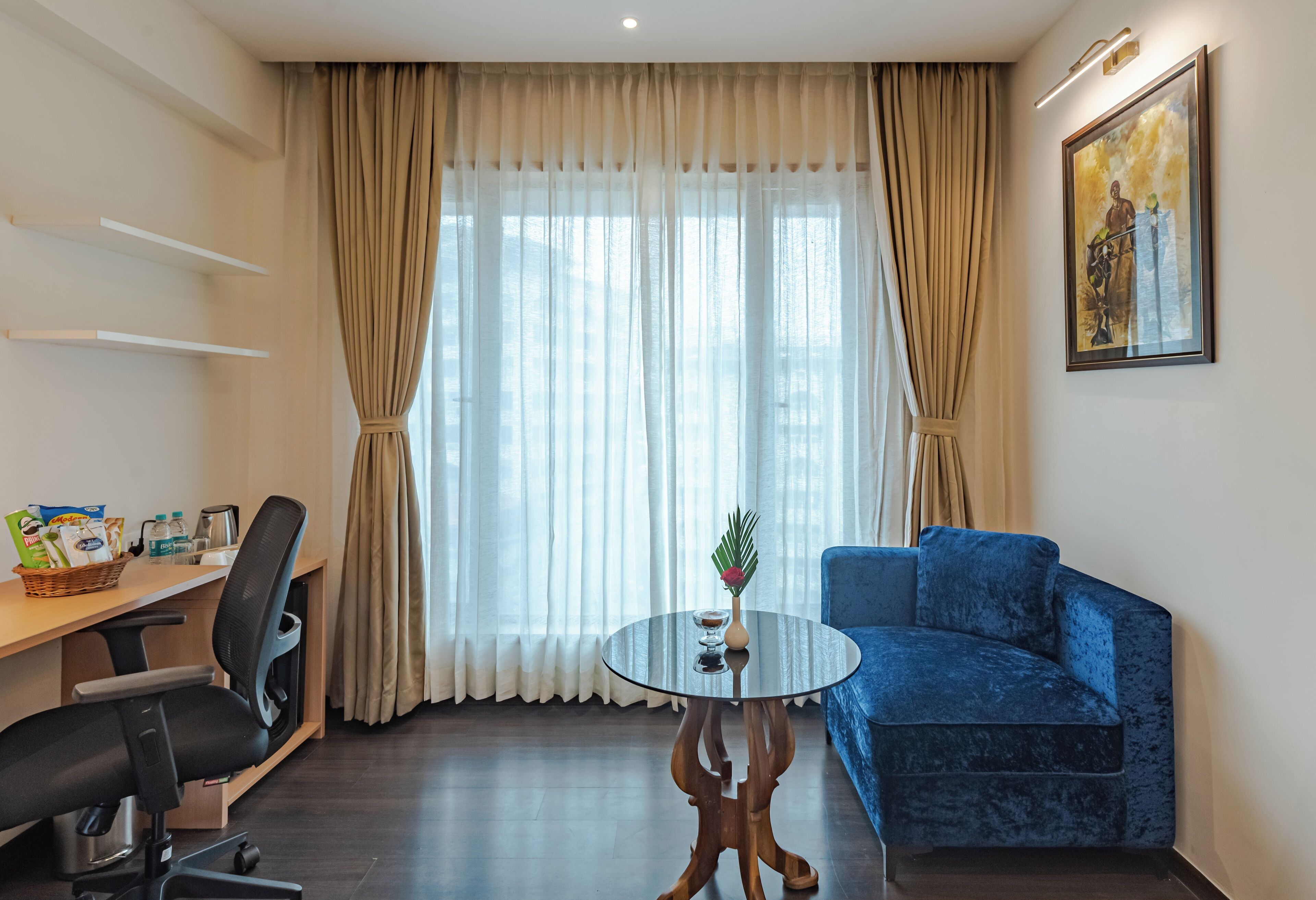 Ein Zimmer mit einem runden Glastisch, einem blauen Sofa, einem Schreibtisch mit Stuhl und einem Fenster mit Vorhängen.