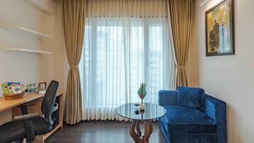 Ein Zimmer mit einem runden Glastisch, einem blauen Sofa, einem Schreibtisch mit Stuhl und einem Fenster mit Vorhängen.