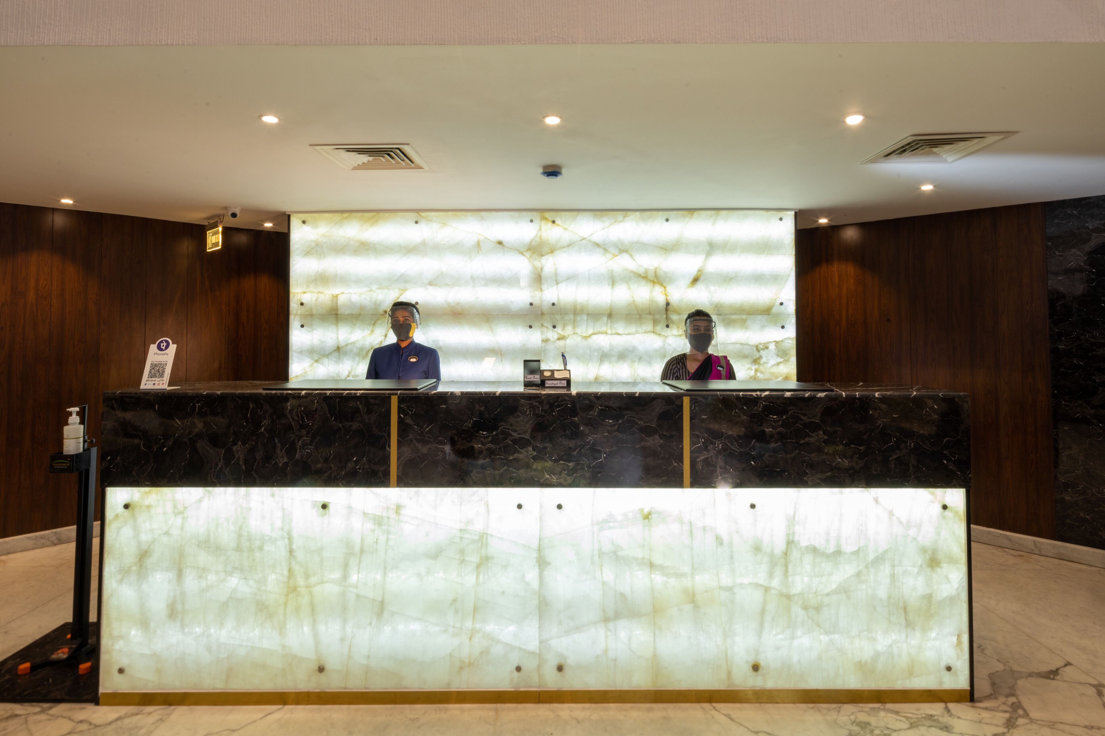 A reception desk with a marble top and a wooden backdrop. There are two receptionists behind the desk.