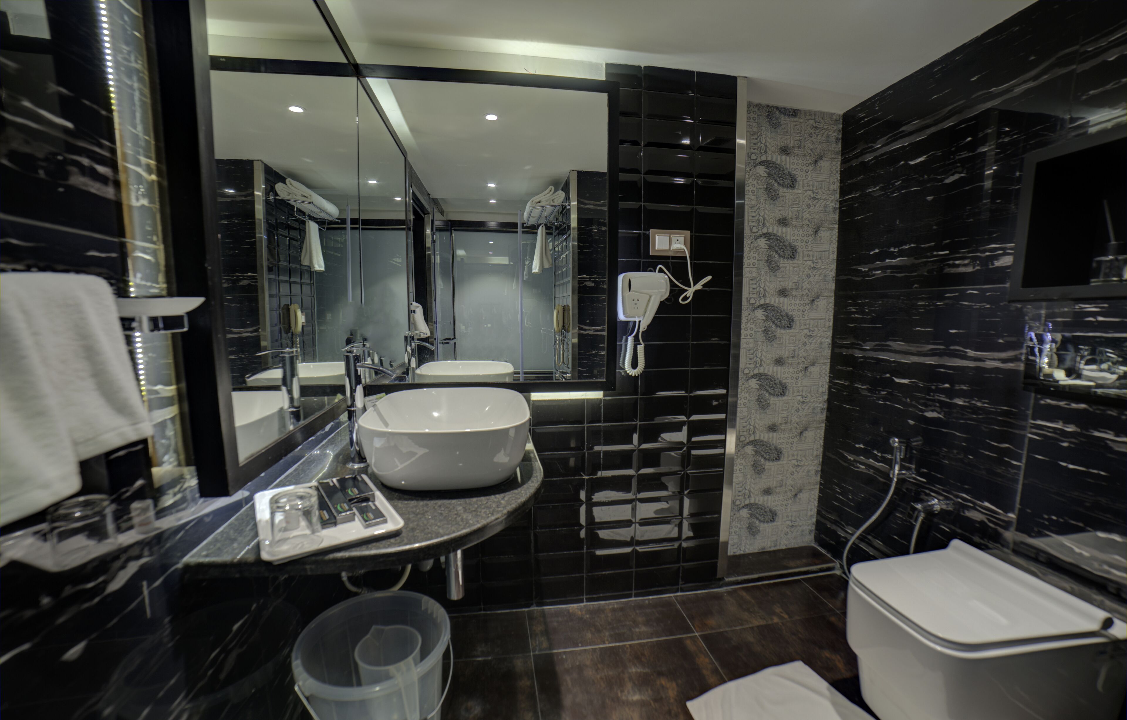 A modern bathroom with a large mirror, two sinks, a toilet, and a shower area.