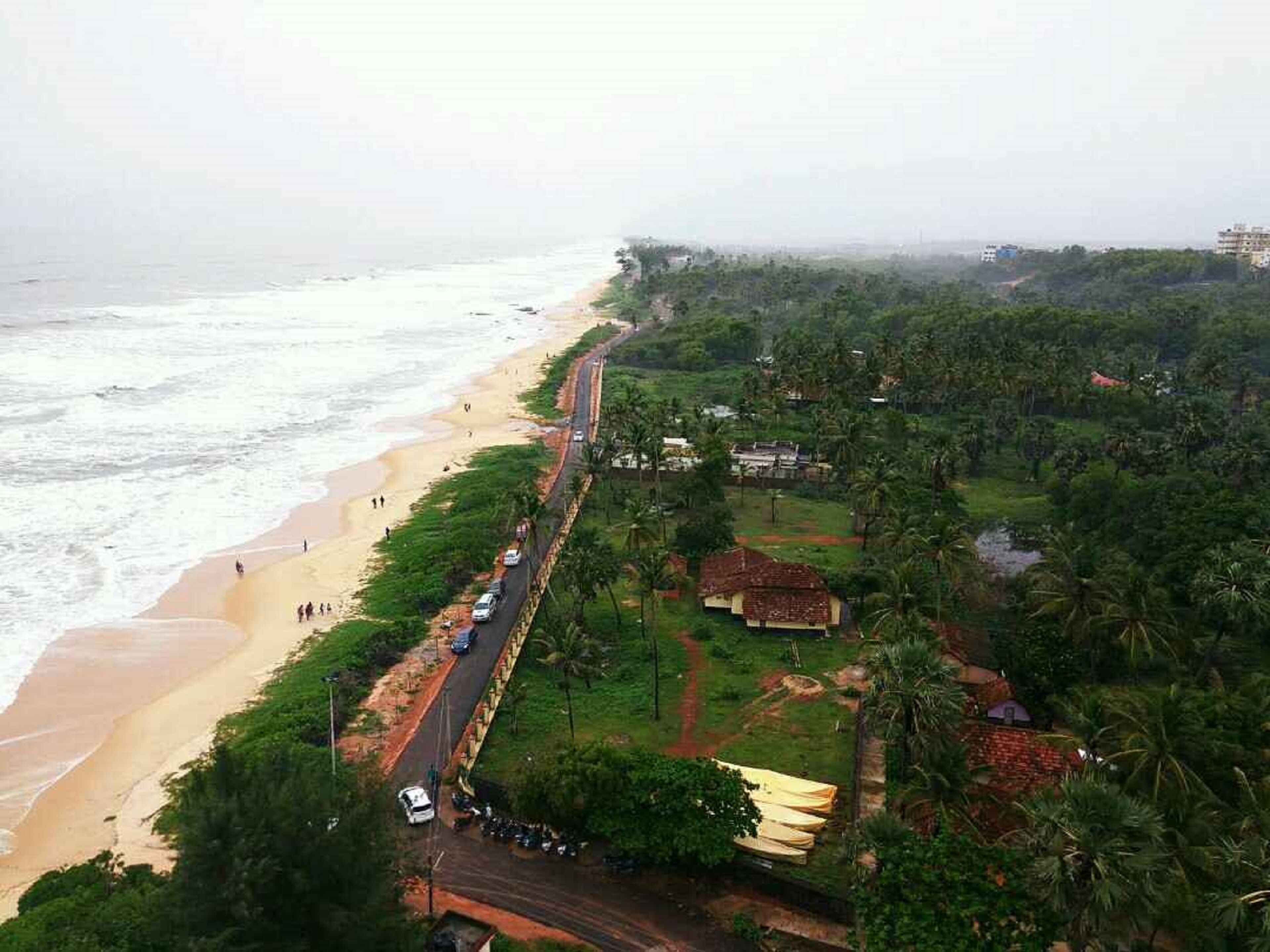 Eine Küstenstraße mit Zugang zum Strand, gesäumt von Grünflächen und Wohngebäuden.