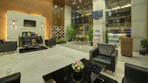 A modern lobby with a marble floor, leather seating, a flat-screen TV, and a reception desk. - Goldfinch Hotel Mangalore (Mangaluru)