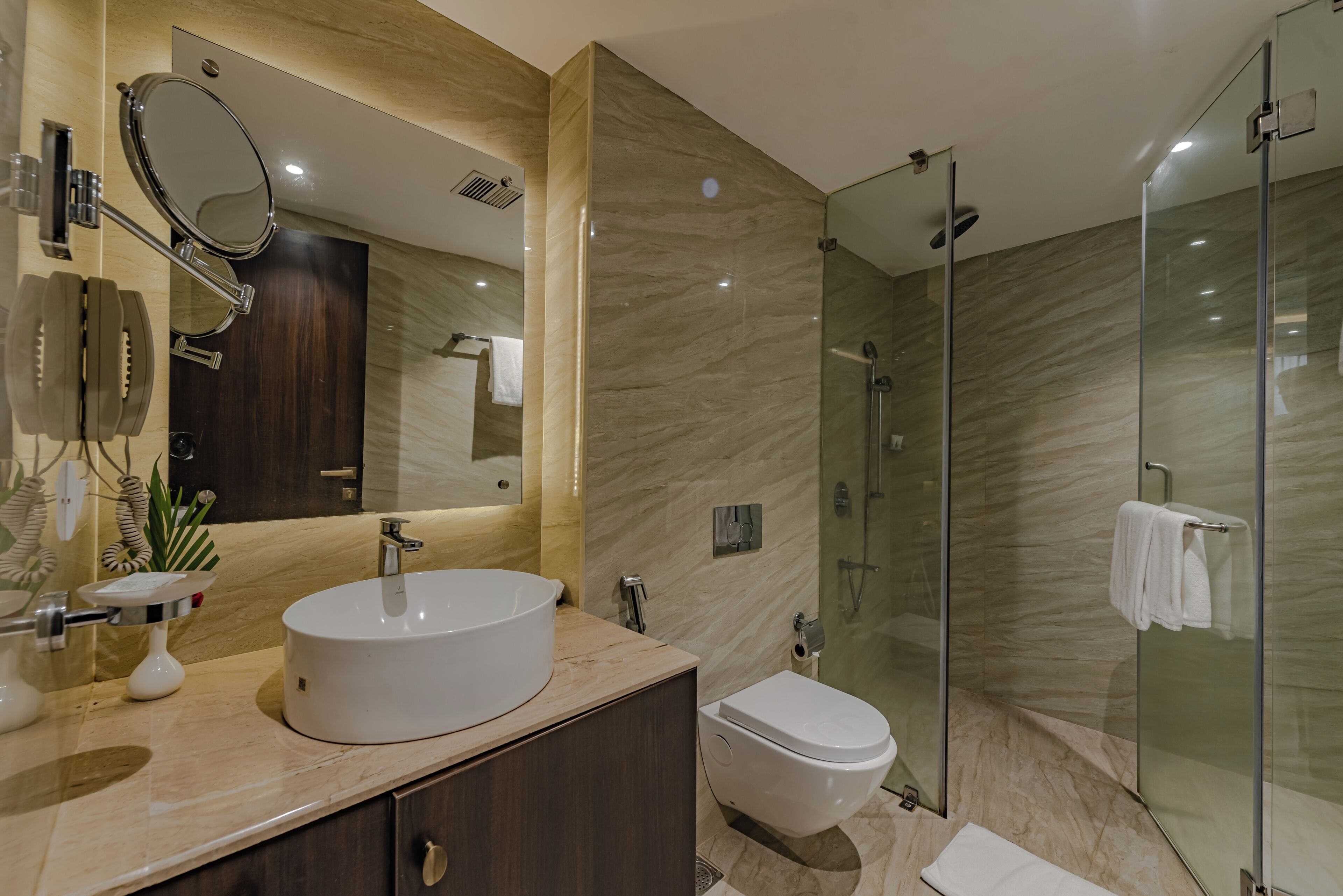 Un baño moderno con un espejo grande, un lavabo redondo, un inodoro y una zona de ducha con mampara de vidrio.