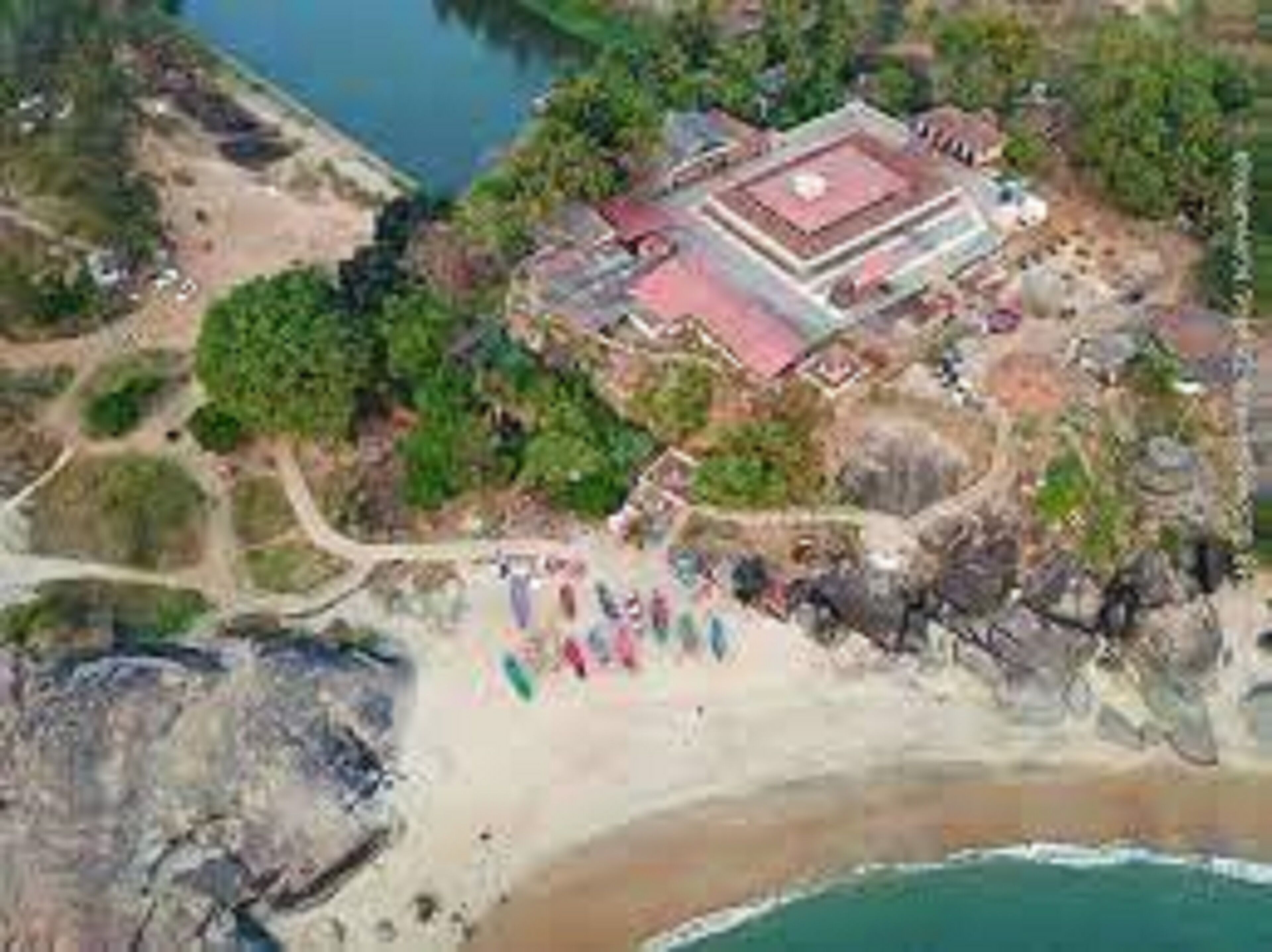 An aerial view of a resort with a large building, a beach, and a rocky shoreline.