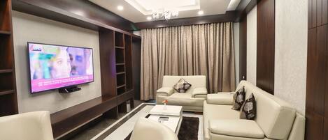 A modern living room with a flat-screen TV, leather sofas, a coffee table, and a chandelier.