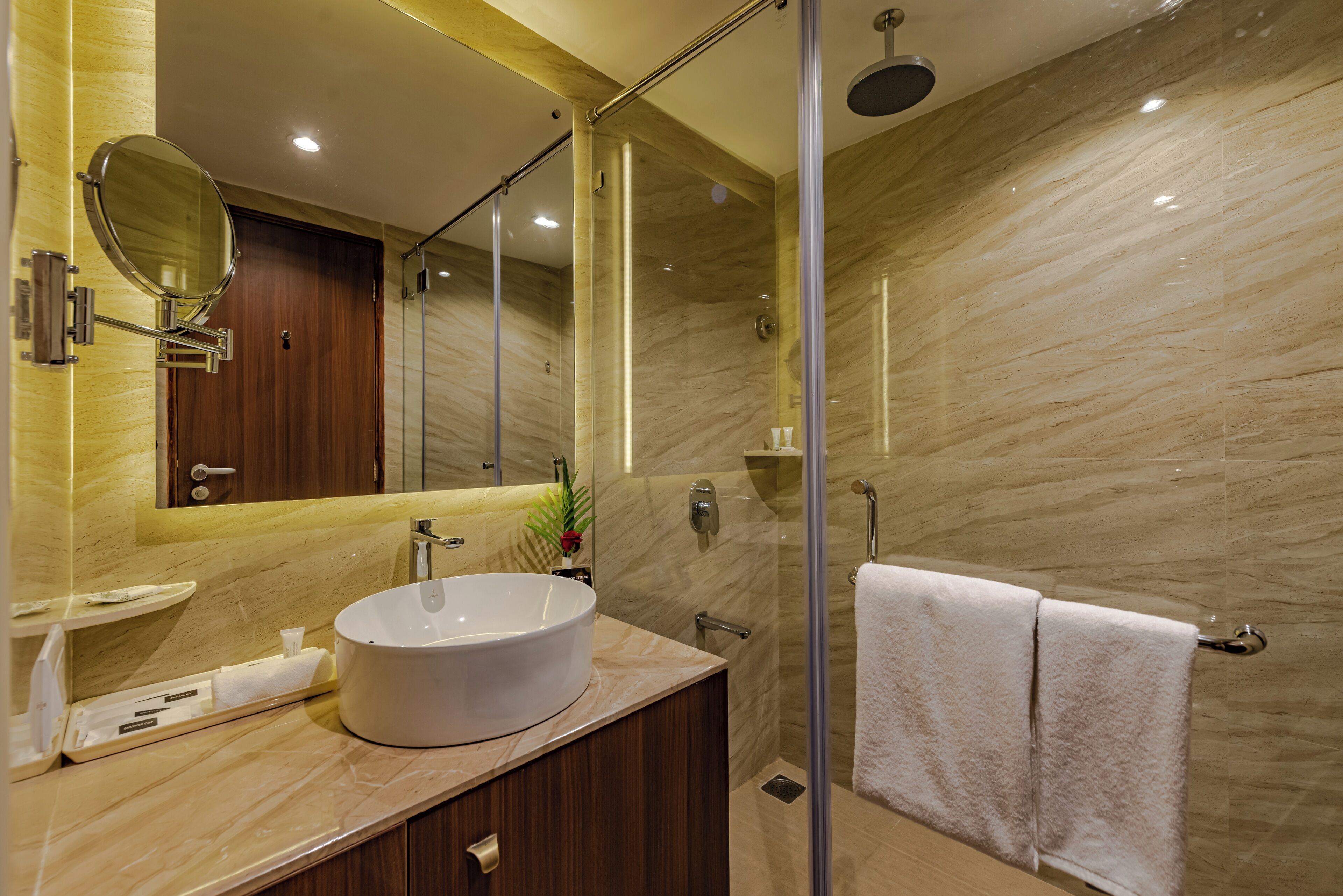 Un baño moderno con un espejo grande, un lavabo redondo y una zona de ducha con mampara de vidrio.