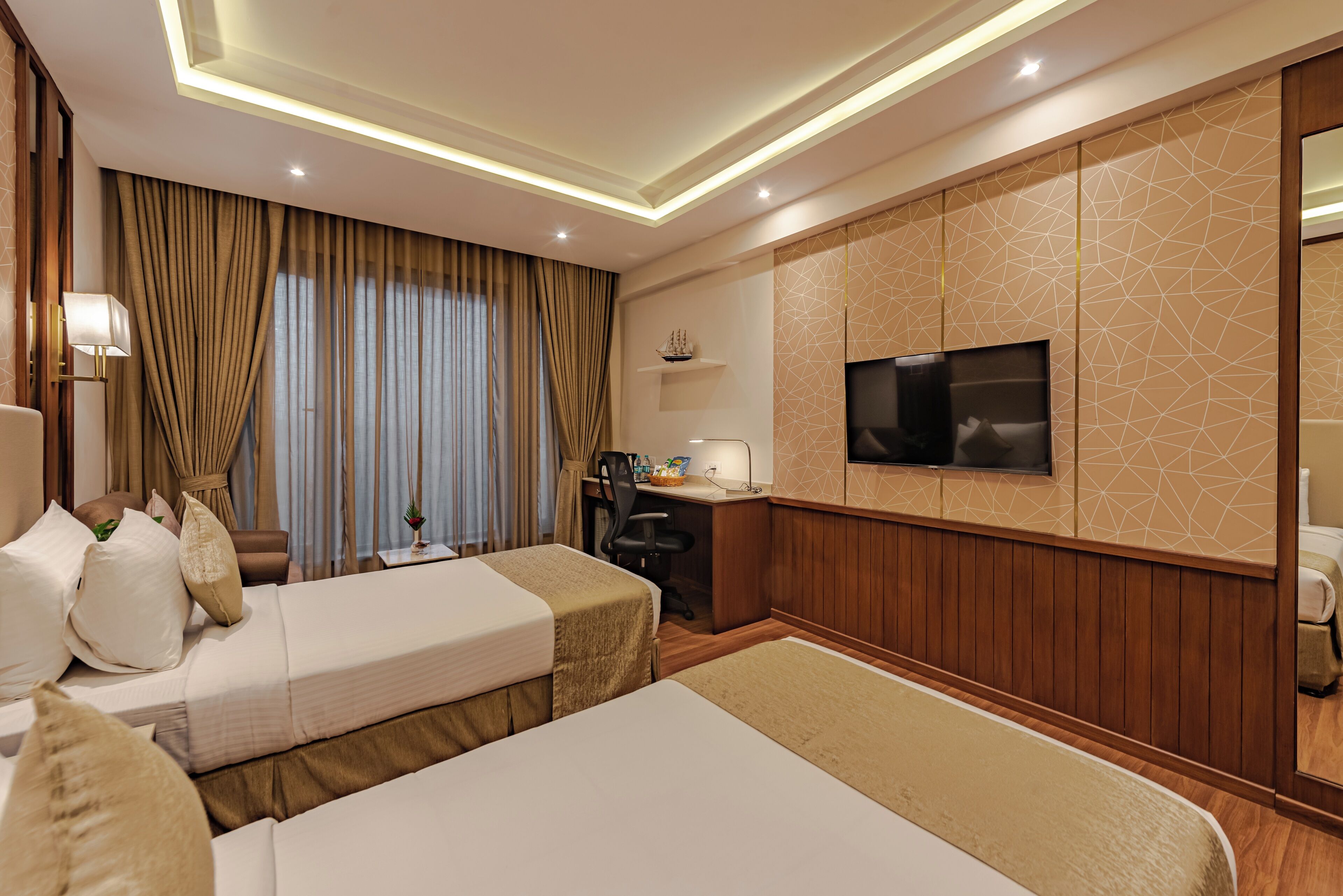A hotel room with two beds, a desk, a chair, a TV, and a small shelf with a ship model.