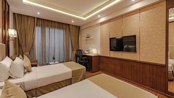 A hotel room with two beds, a desk, a chair, a TV, and a small shelf with a ship model.