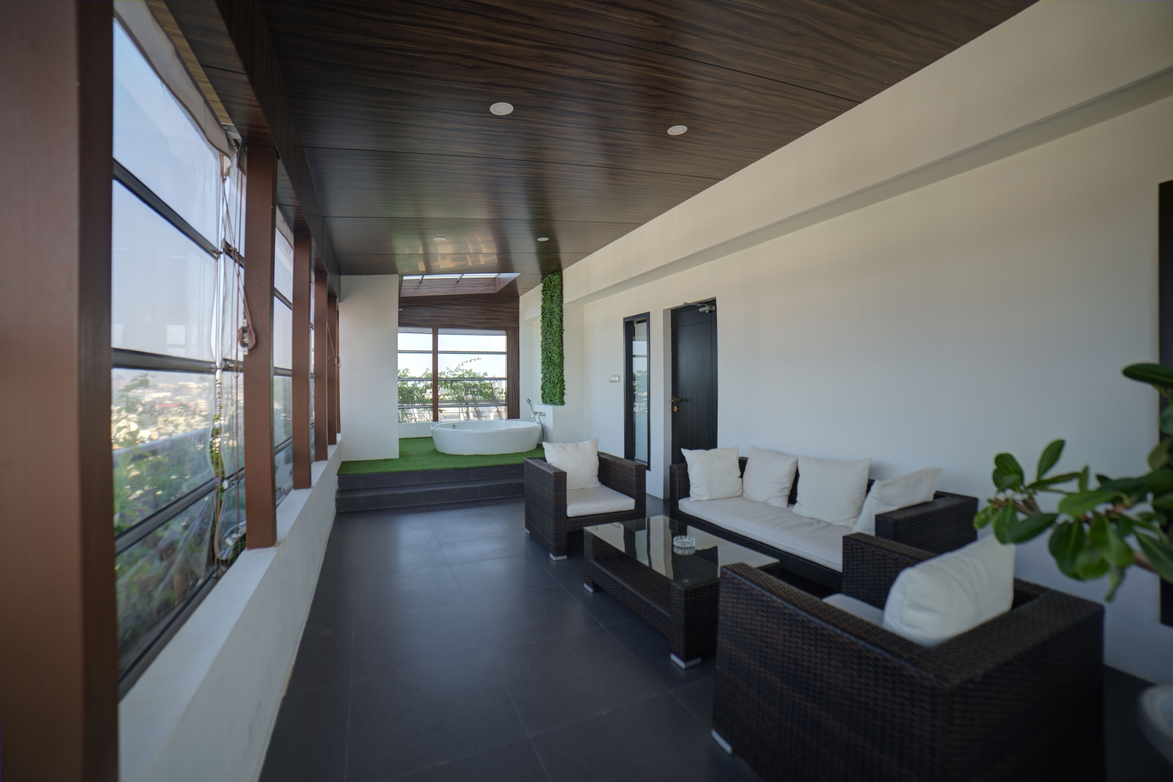 A modern outdoor seating area with wicker furniture and a glass table, overlooking a green landscape.