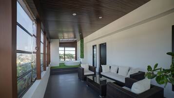 A modern outdoor seating area with wicker furniture and a glass table, overlooking a green landscape.