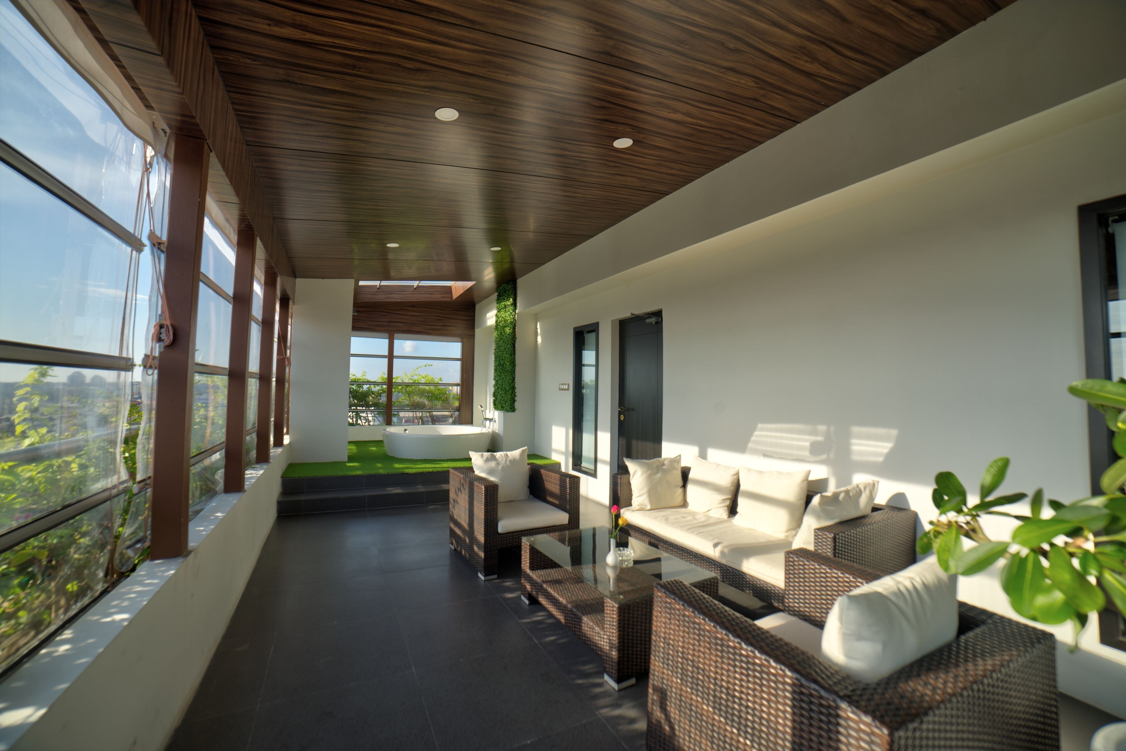 A modern outdoor seating area with wicker furniture and a glass table, overlooking a lush garden and cityscape.