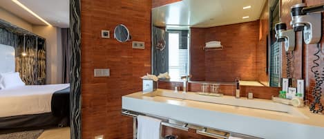 A modern hotel room with a wooden wall, a large mirror, a white sink, and a bed.
