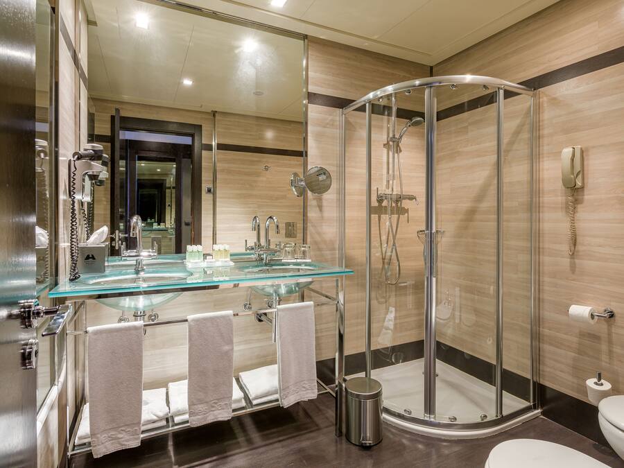 A modern bathroom with a glass shower enclosure, a glass sink, and a toilet.