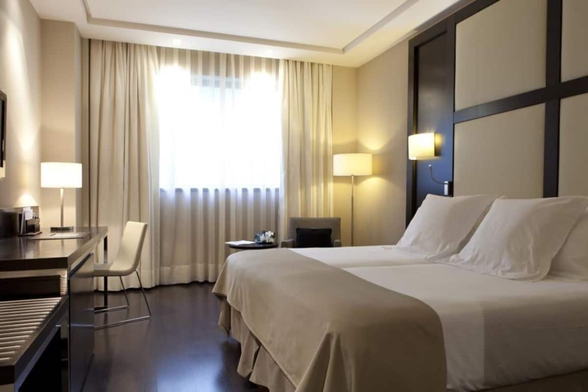 A hotel room with a bed, a desk, a chair, and a lamp.