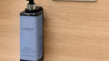 Botella de jabón para manos y cuerpo etiquetada 'LANVIN Paris' sobre una superficie de madera, con un cartel sobre prácticas de sostenibilidad.