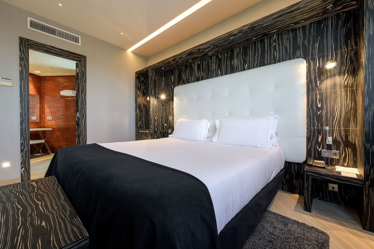 Una habitación de hotel moderna con una cama grande, un revestimiento de madera y un baño separado visible a través de una puerta.