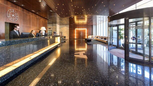 A modern hotel lobby with a reception desk, seating area, and a large clock on the wall.