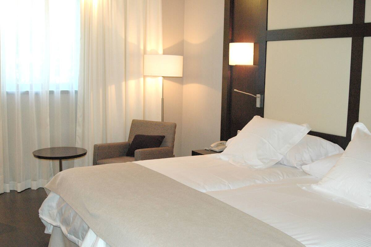 A hotel room with a large bed, a chair, a small table, and a lamp.
