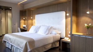 A modern hotel room with a large bed, bedside tables, a desk, and a mirror.