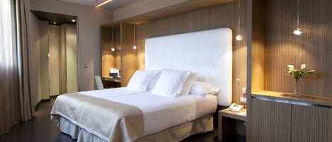 A modern hotel room with a large bed, bedside tables, a desk, and a mirror.