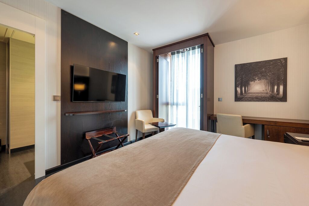 Una habitación de hotel moderna con una cama grande, un televisor de pantalla plana montado en la pared, un escritorio pequeño y una silla.