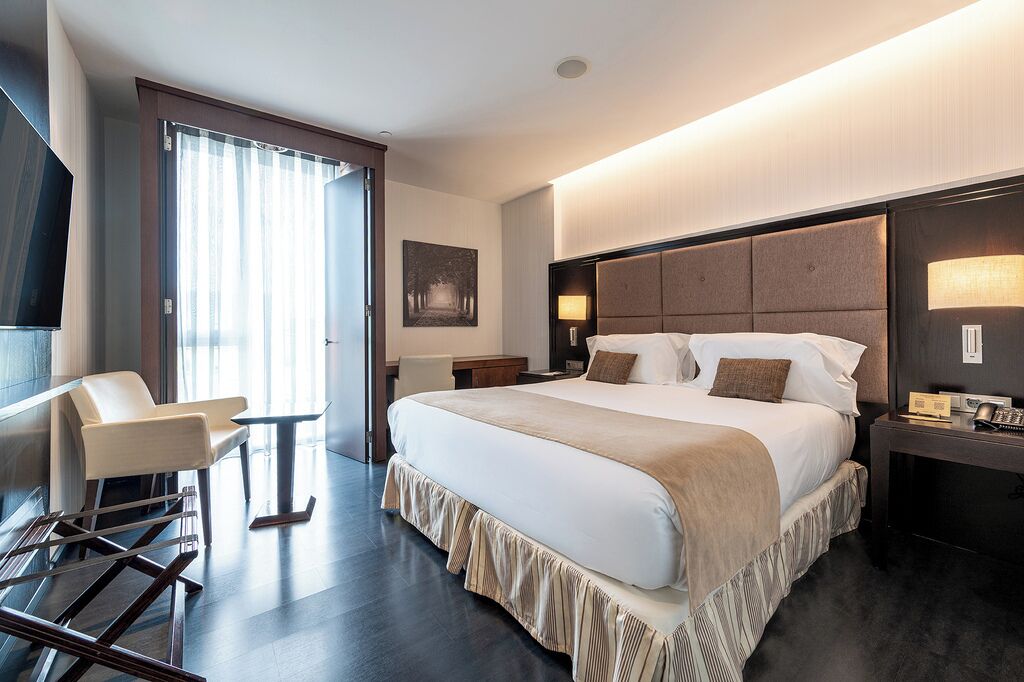 A hotel room with a large bed, a desk, a chair, and a television.
