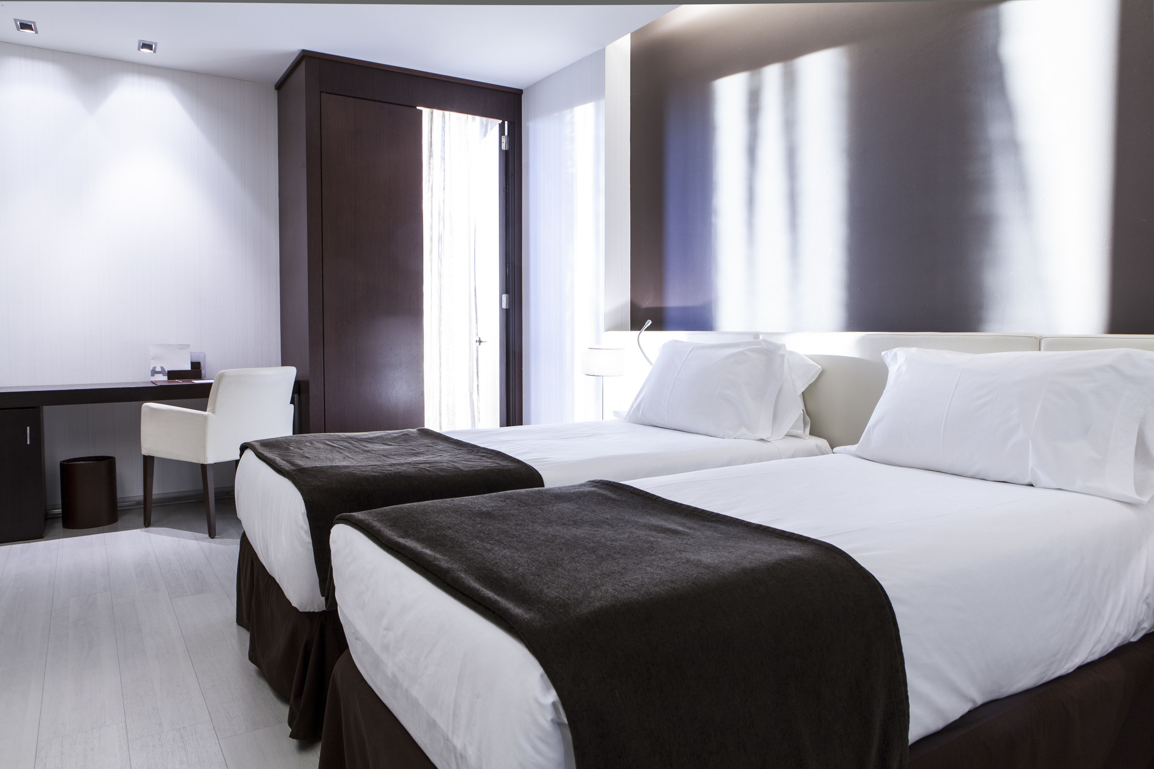 A hotel room with two beds, a desk, and a chair.