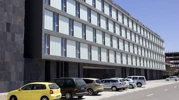 A modern hotel building with multiple floors, large windows, and a parking area with several cars.