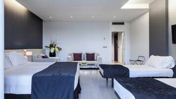 A modern hotel room with two beds, a sofa, a coffee table, and a TV.