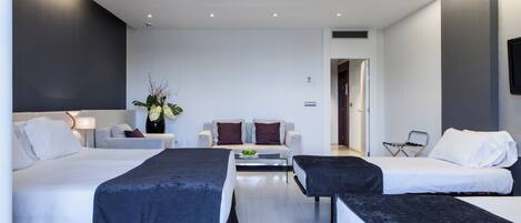 A modern hotel room with two beds, a sofa, a coffee table, and a TV.