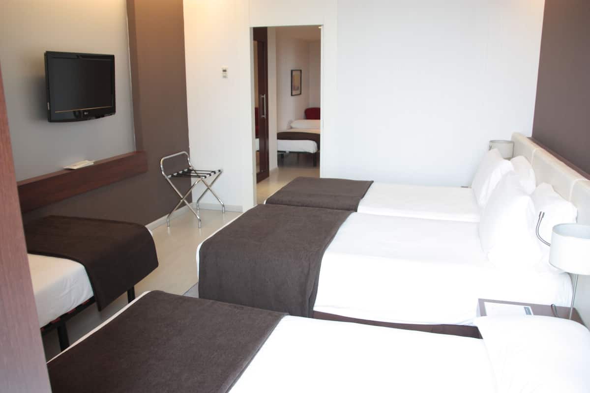 A hotel room with three single beds, a TV mounted on the wall, a chair, and a door leading to another room.