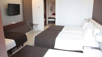 A hotel room with three single beds, a TV mounted on the wall, a chair, and a door leading to another room.