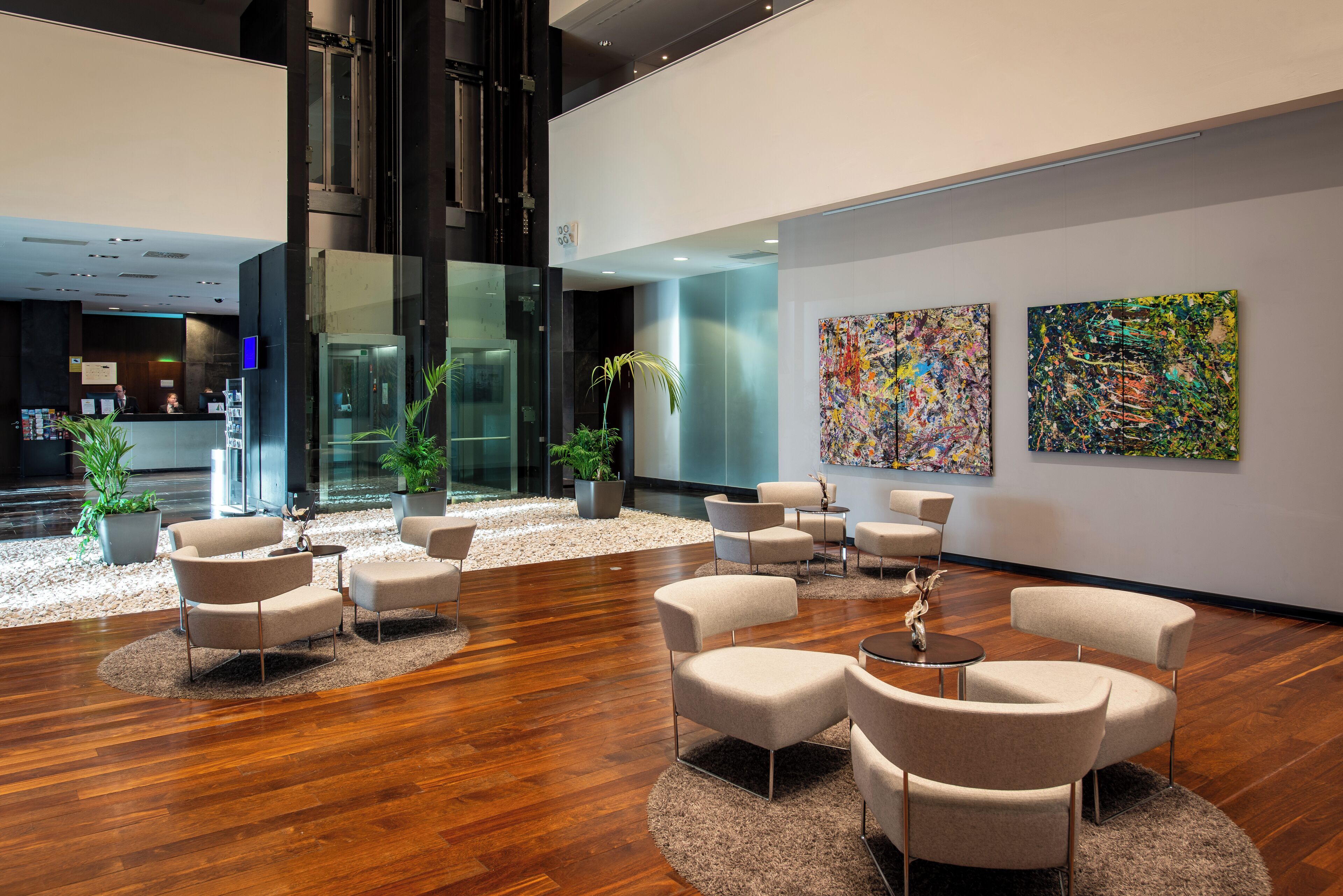 A modern lobby with a wooden floor, beige chairs, and abstract paintings on the walls.