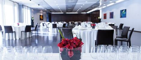 Un salón de banquetes con mesas dispuestas para un evento formal, con un centro de mesa de flores rojas en una jarra de vidrio.