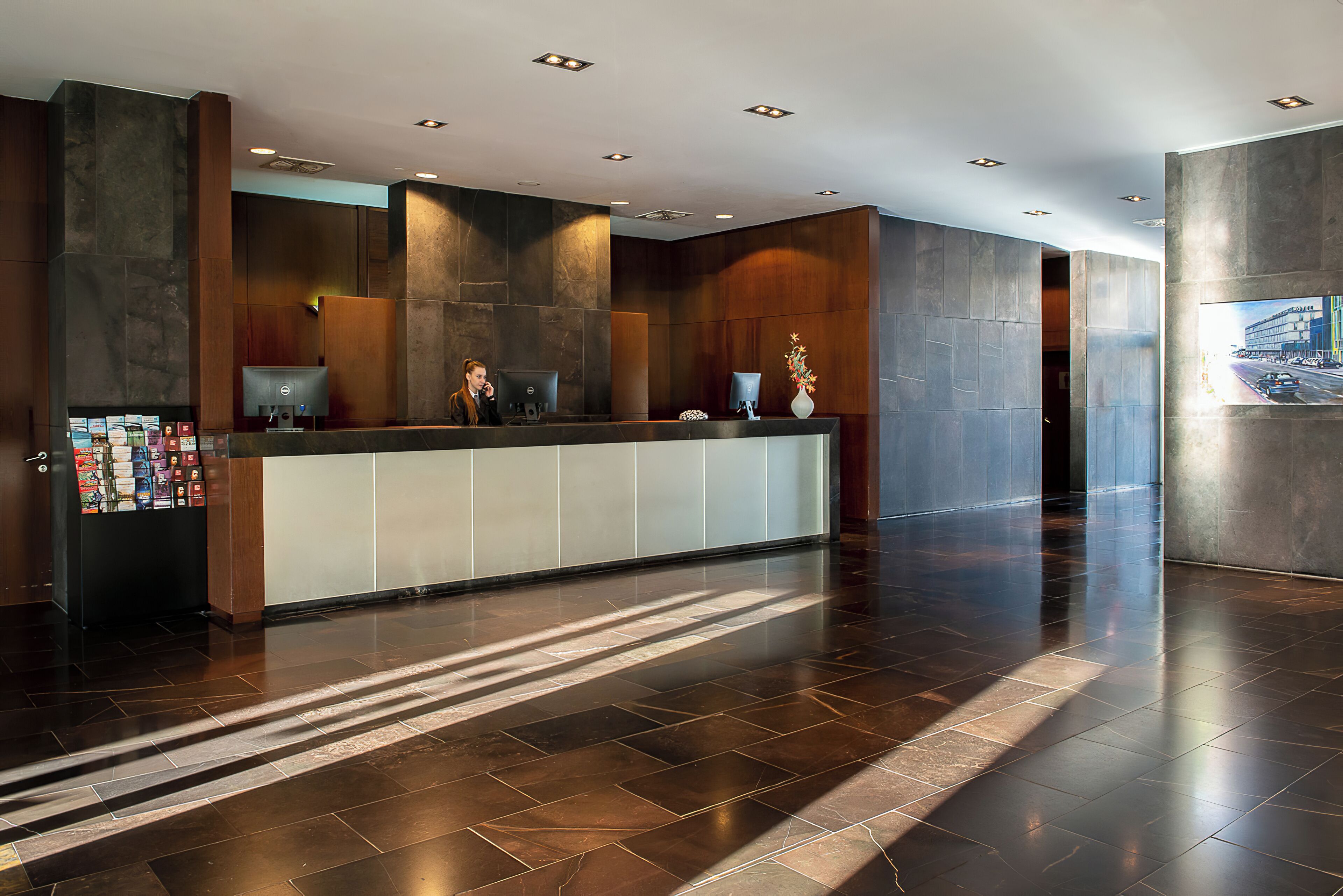 A modern reception area with a marble reception desk, a digital information kiosk, and a large poster on the wall.
