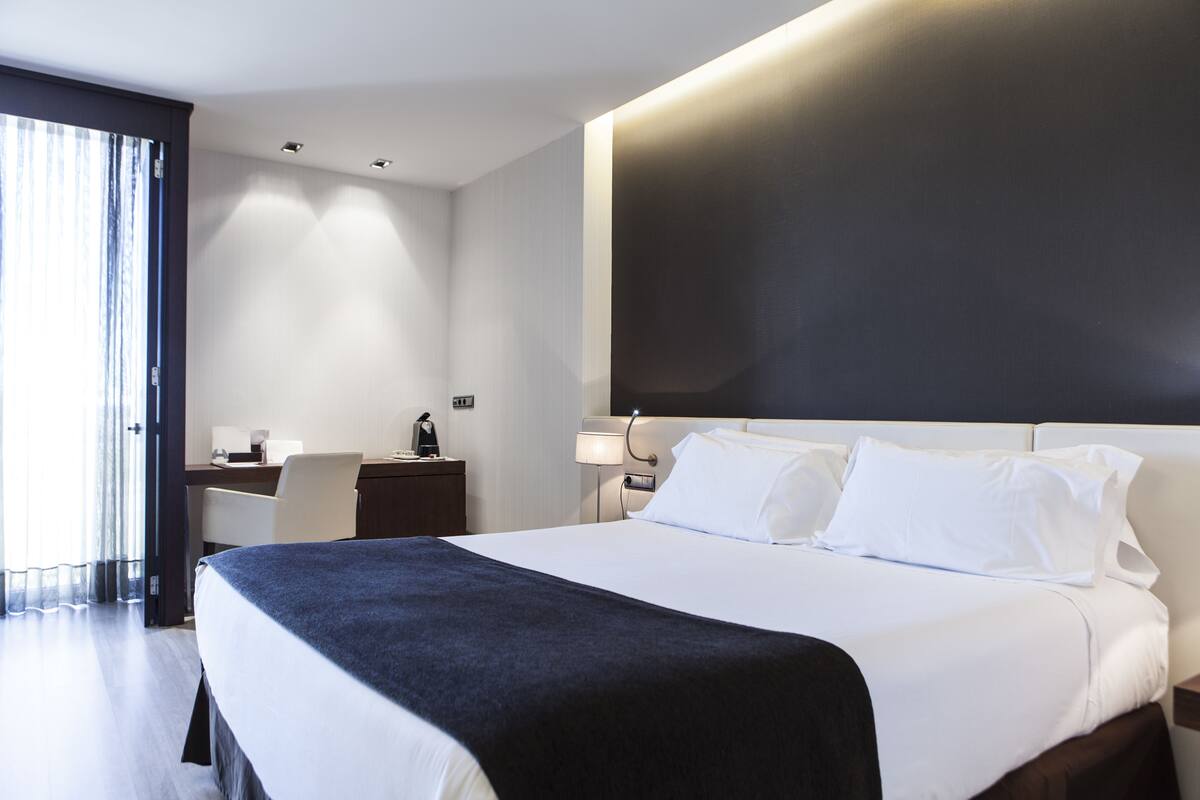 A modern hotel room with a large bed, a desk, and a chair.