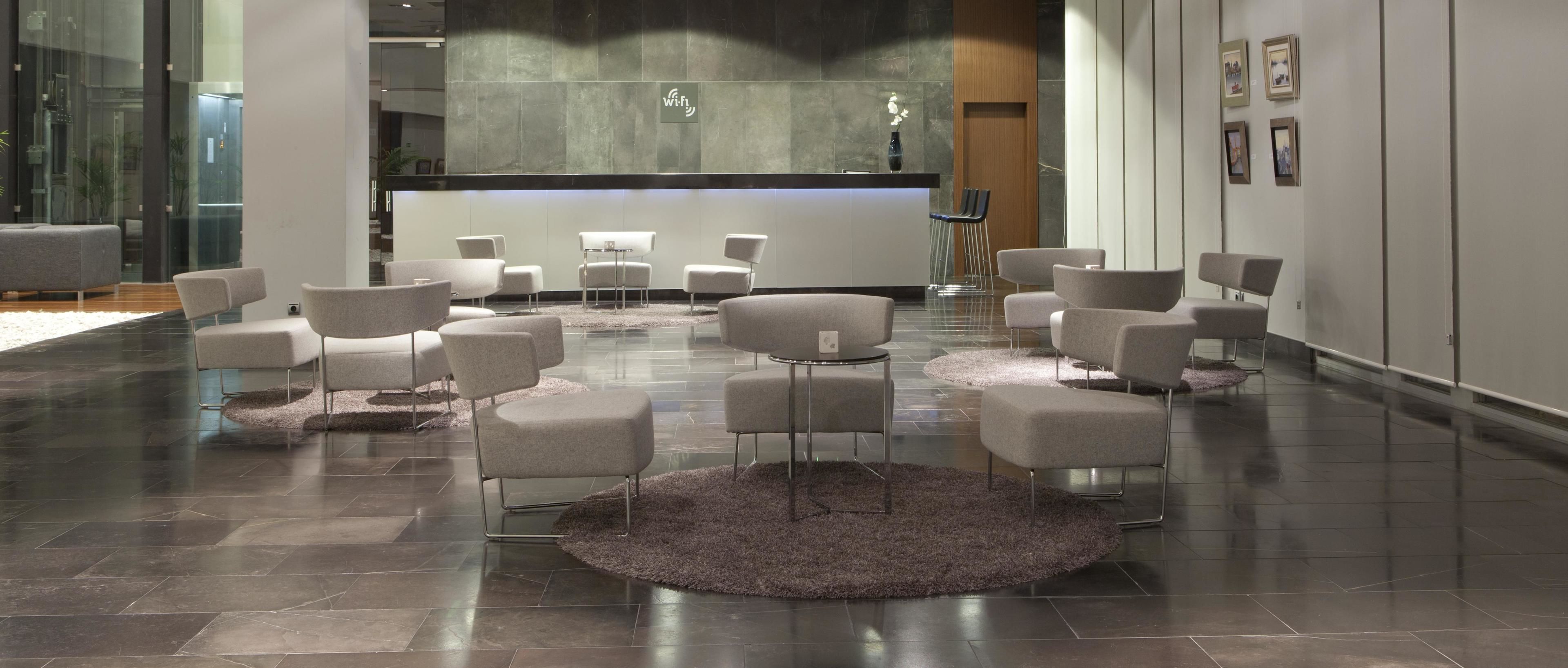 A modern lobby with a reception desk, several seating areas, and a large rug on the floor.