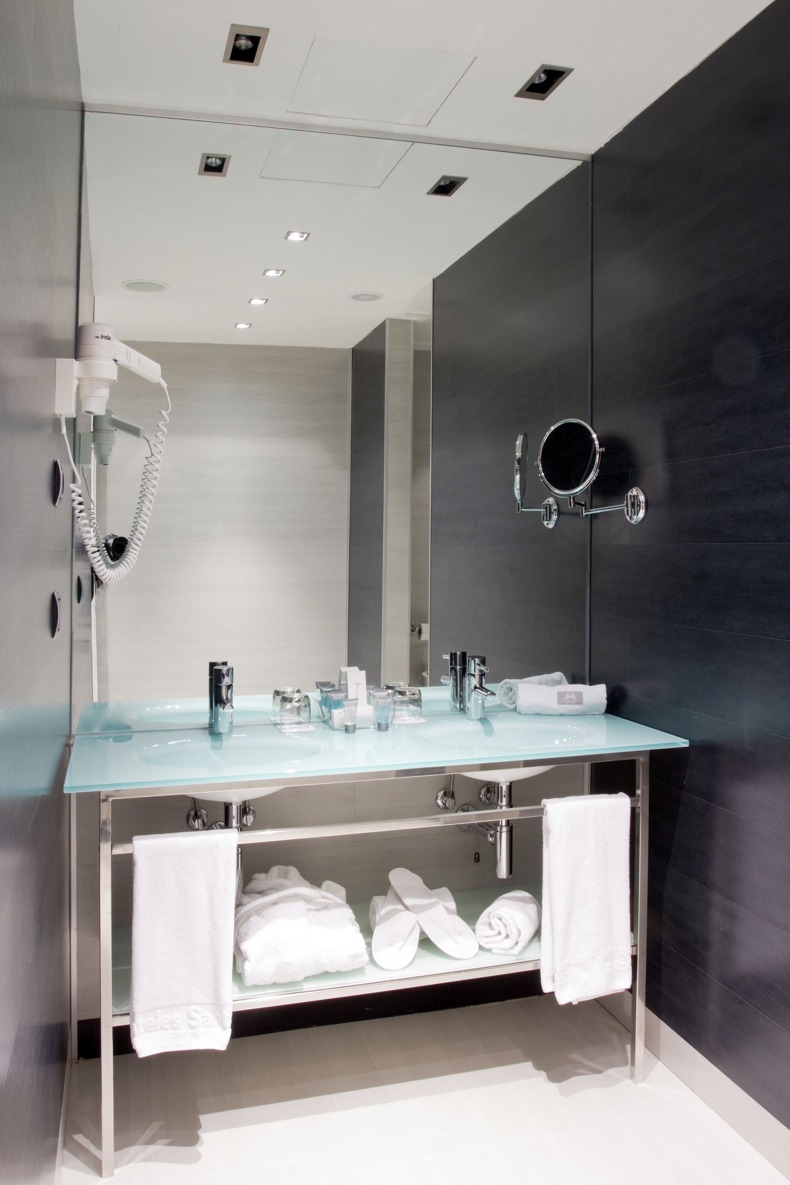 Une salle de bain moderne avec un lavabo en verre, un grand miroir, un sèche-cheveux et un porte-serviettes.