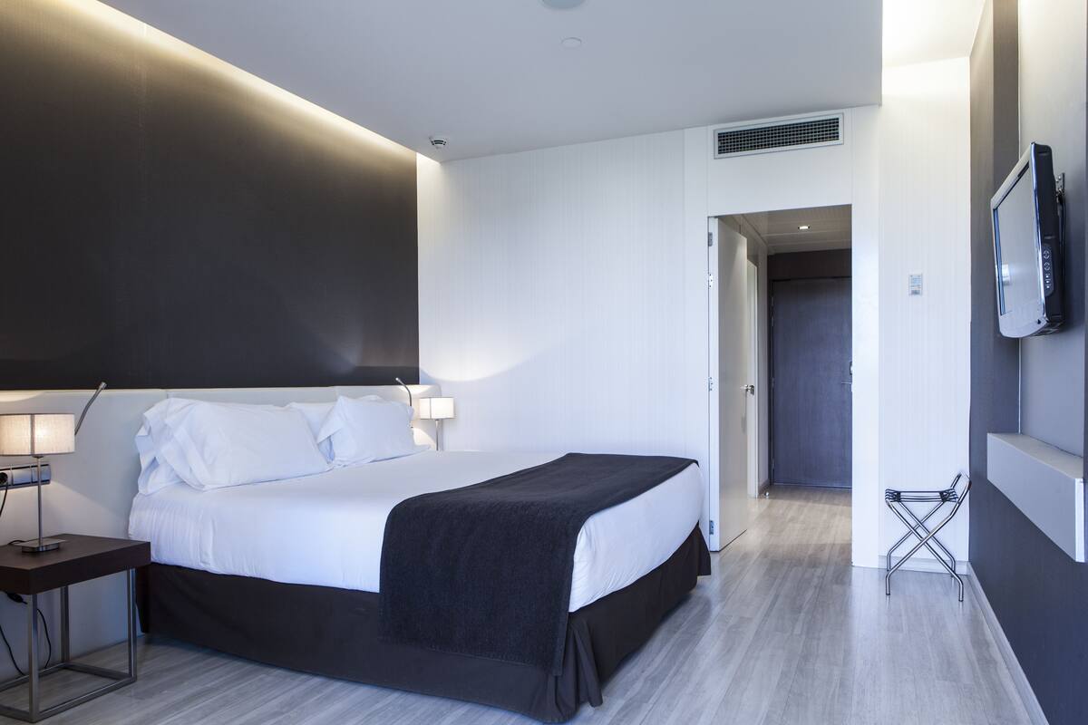 A modern hotel room with a large bed, bedside lamps, a flat-screen TV, and a walk-in closet.