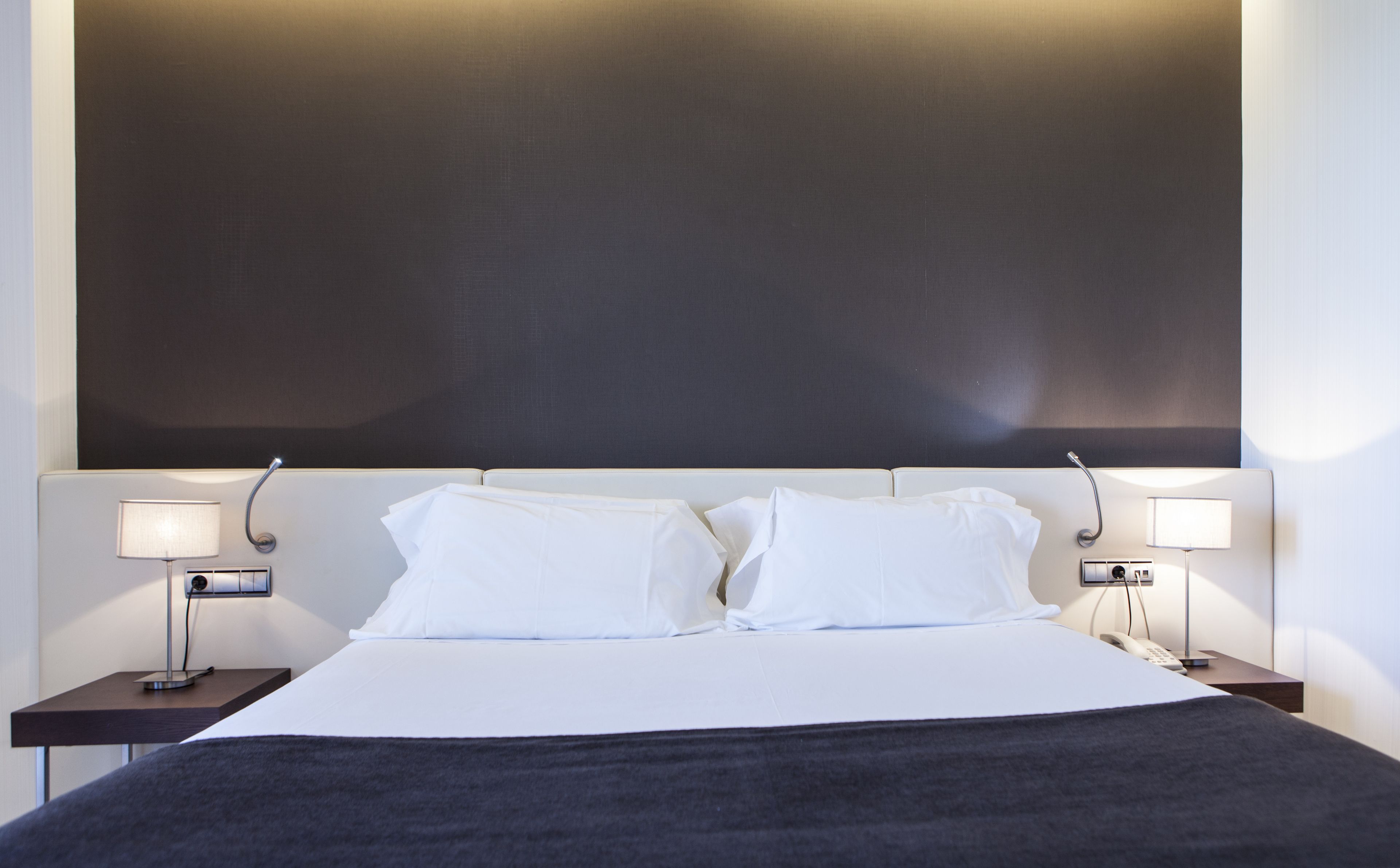 A neatly made bed with white linens and a dark throw blanket, flanked by two bedside tables with lamps.